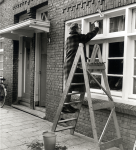 125754 Afbeelding van een vrouw op een trap tijdens het lappen van de ramen van het huis Boomstraat 9 te Utrecht.N.B. ...